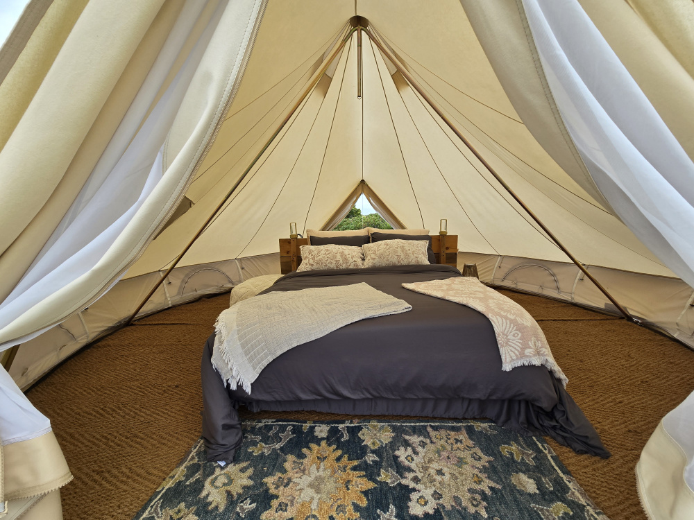 Inside a yurt at Highland Hideaway. A bed with blue sheets and brown floor. 