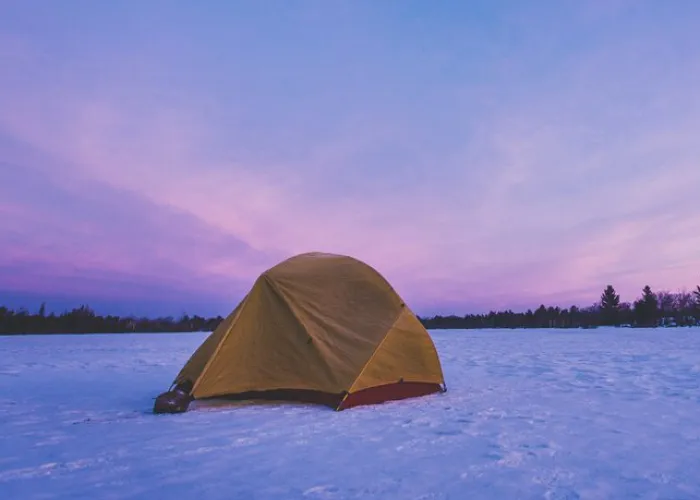Winter camping image of a tent on snow with pink and blue sky. Image credit to DESTINATION ONTARIO