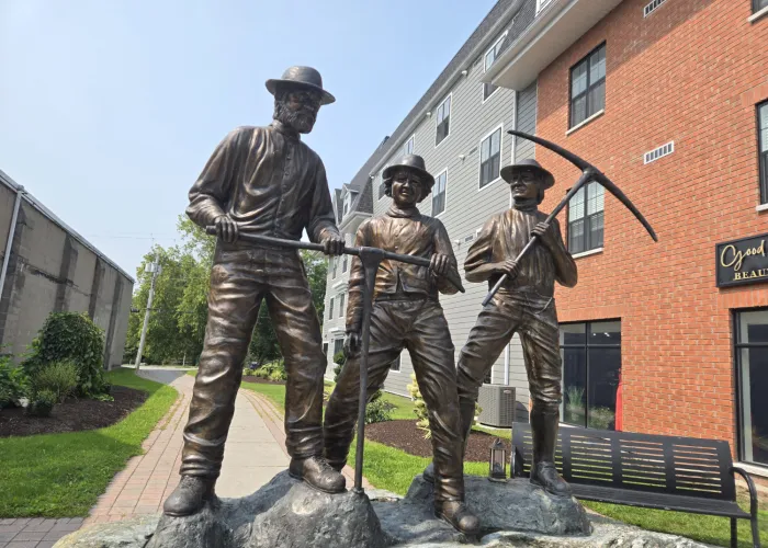 Marmora Miners' Statue, depiction of three people standing on a large rock with mining tools. The people in the statue are made of brass.